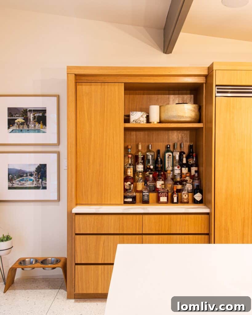 A modern kitchen with a large white island featuring a 'pivot bar' and built-in icemaker, facing a liquor cabinet, perfect for entertaining.