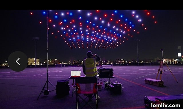 A large crowd gathers in a park, eagerly watching a vibrant drone light show illuminating the dark sky with colorful patterns.