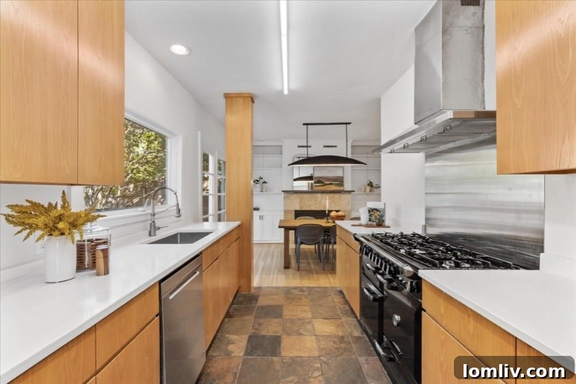 A sun-drenched, modern kitchen with white cabinetry, a large picture window over the sink overlooking a lush garden, and a distinctive red AGA range, emphasizing contemporary design and functionality.