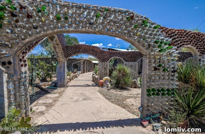Another perspective of the unique bottle house facade, illustrating the craftsmanship and the artistic arrangement of recycled glass bottles catching the sunlight.