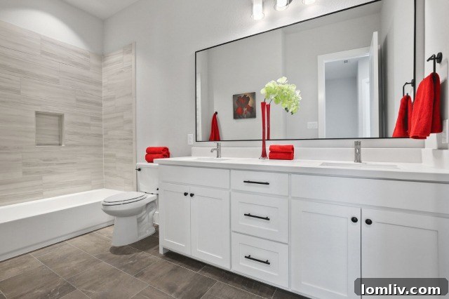 Secondary bathroom with dual sinks, white Shaker-style cabinets, and large-format tile
