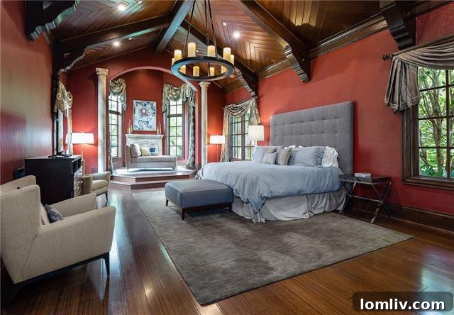 The master bedroom at 5019 Shadywood Lane, showcasing a chevron-patterned wood floor, vaulted beamed ceiling, and an elevated sitting area with a cast stone fireplace.
