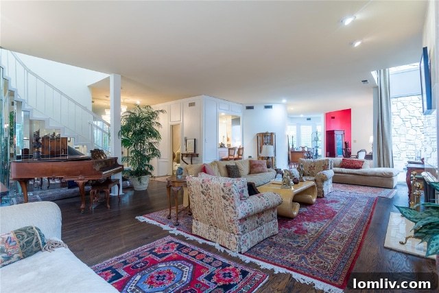 Expansive and bright living room of Unit 2B, featuring a Wurlitzer baby grand piano, oriental rugs, a wet bar, and views into a rounded dining area and kitchen beyond