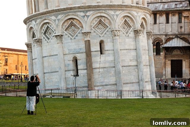 A striking black and white photograph of the Leaning Tower of Pisa, captured from a unique angle that emphasizes its iconic tilt and architectural details.