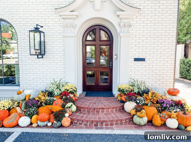 A professional fall display by Lawns of Dallas, showcasing layered pumpkins, hay bales, and vibrant fall plants around a front door.