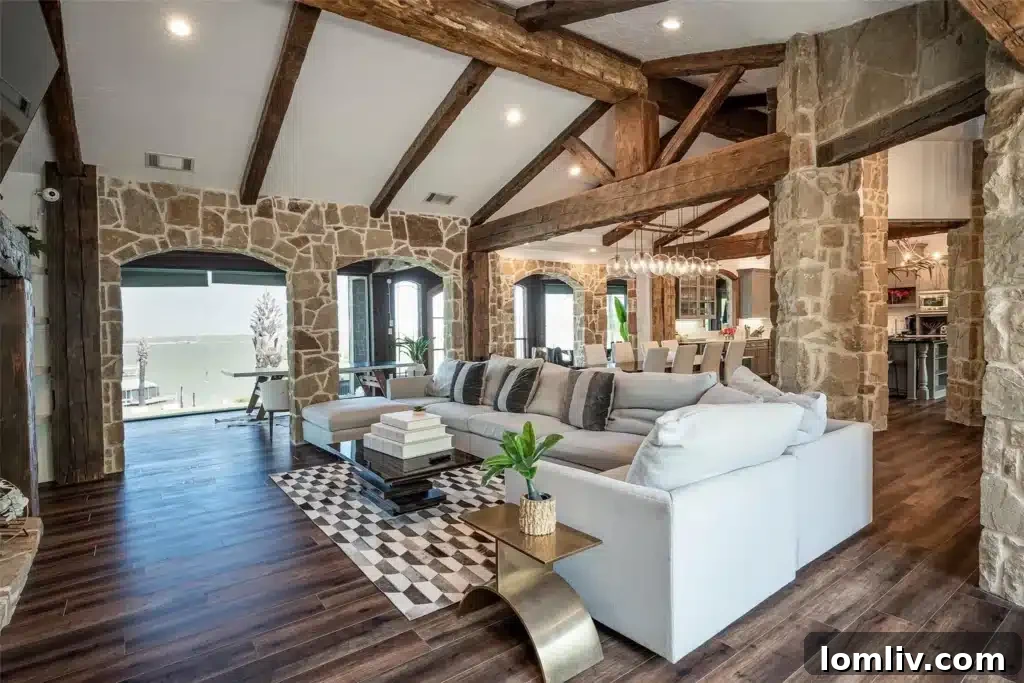 View of the open-concept living area with a large stone fireplace, vaulted wooden ceilings, and natural stone walls, seamlessly connecting to the dining and kitchen areas.