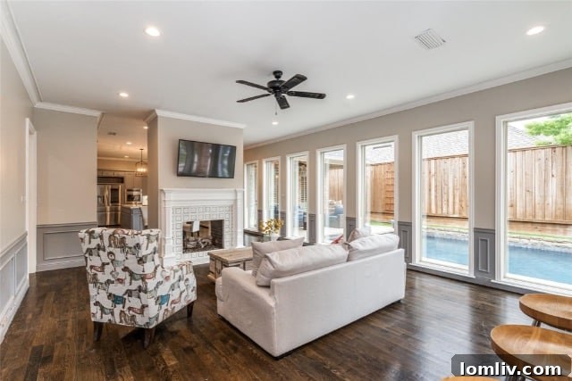 Spacious living room with dark hardwood floors, neutral decor, and floor-to-ceiling windows overlooking a swimming pool.