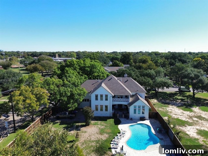 Resort-style beach entry pool surrounded by mature trees in the backyard of Midway Hills Modern Tudor