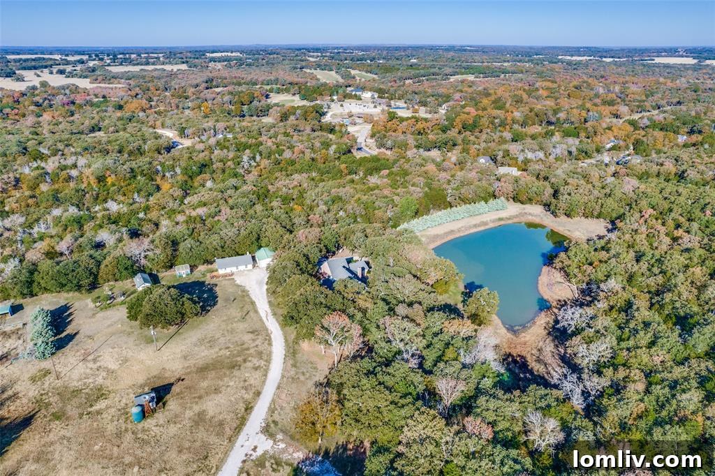 Expansive outdoor deck complete with a rustic fireplace, offering stunning views of a large private pond and beautifully landscaped gardens, perfect for entertaining.