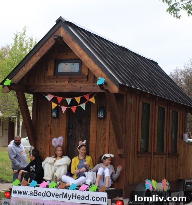 A charming tiny home, 112 square feet, being towed during the Hollywood Heights Newellian Easter Parade, symbolizing sustainable living and the growing tiny house movement.