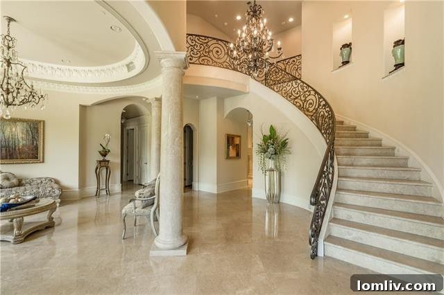 A grand double-height entryway with a sweeping staircase featuring custom iron balustrades and luxurious Syrian marble floors, showcasing the home's architectural elegance.