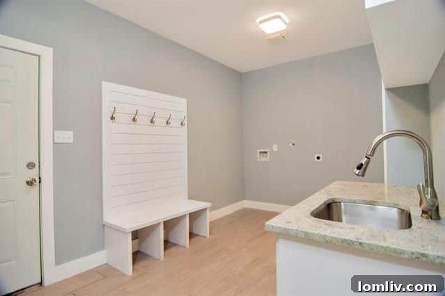 Functional and stylish laundry room featuring hook-ups, ample cabinetry with a sink, and a charming built-in bench with coat hooks