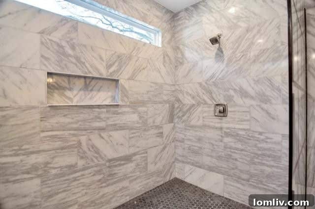 Sophisticated freestanding soaking tub set against floor-to-ceiling tilework, within the spacious walk-in shower of the luxurious master bath
