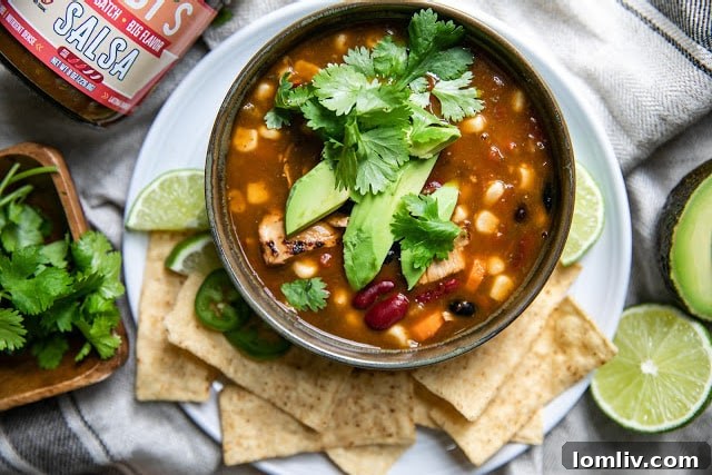 A vibrant bowl of ZUBI'S Chicken Tortilla Soup generously garnished with fresh avocado slices, chopped cilantro, and crispy tortilla strips, ready to be enjoyed.