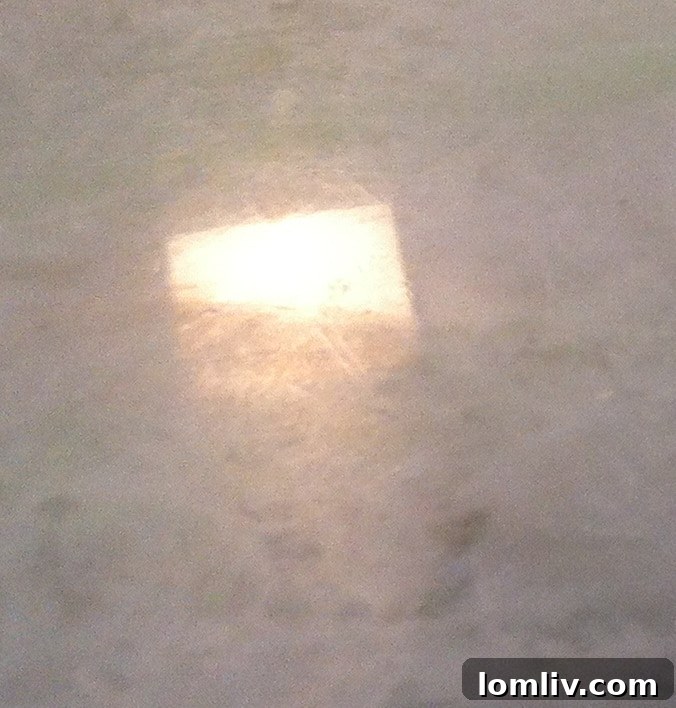 An etched stone surface displaying a visible dull area and distorted reflection, indicating damage from acidic contact, typically on a kitchen countertop.