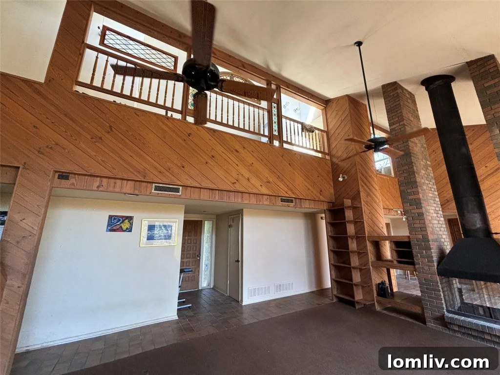 The striking interior of the 1970s shed-style home, featuring a towering stone fireplace, soaring ceilings, and expansive windows.