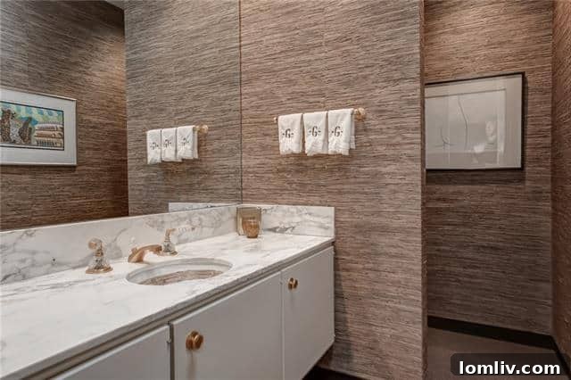 Stylish powder room featuring grasscloth wallpaper, Carrara marble, and brass fixtures.